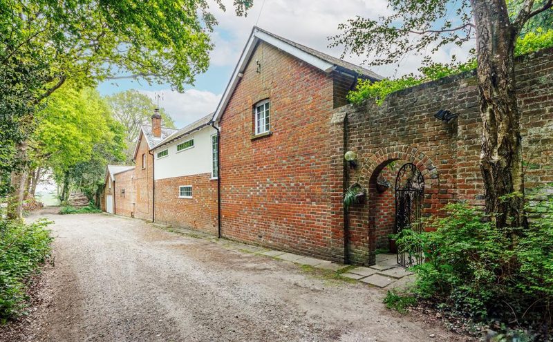 A gravel track running past a brick outbuilding and an old garden wall with a wrought-iron gate, trees overhead.