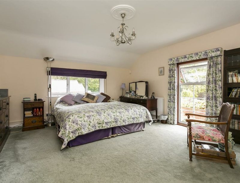A large bedroom with a double bed, dressing table and windows on two sides.