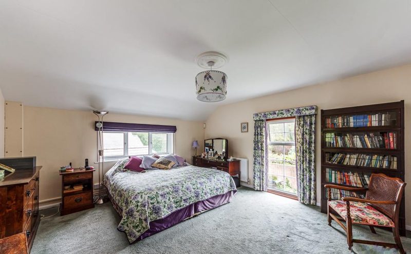 A bedroom with a double bed, bookcase and a glazed door letting in daylight.