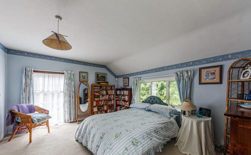 A pale blue bedroom with a double bed and windows on two walls.