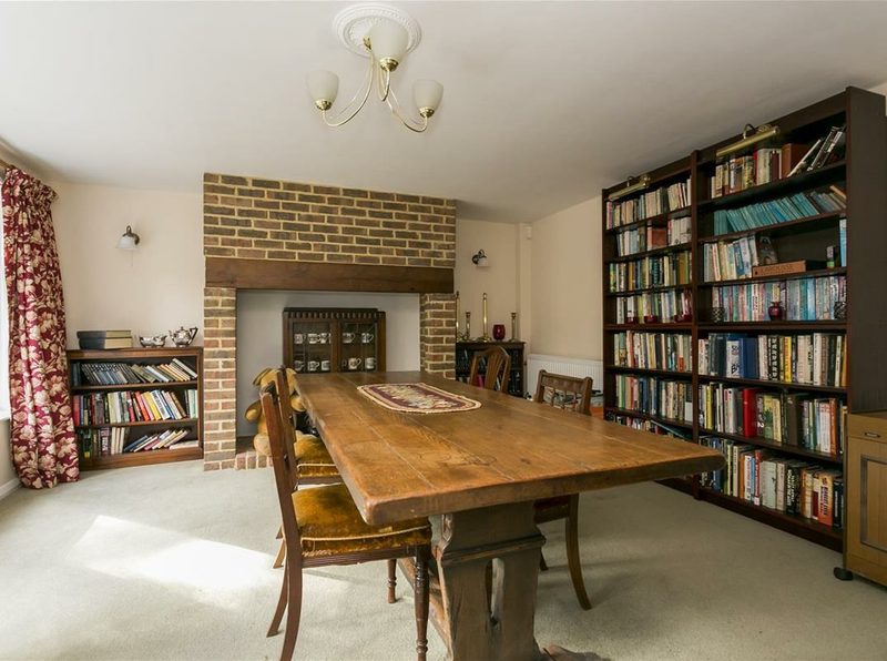 A ground-floor room with an exposed brick fireplace, bookshelves and a long wooden table.