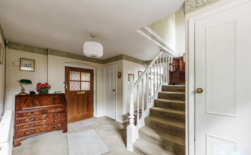 An entrance hall with a wooden front door, chest of drawers and a carpeted staircase.