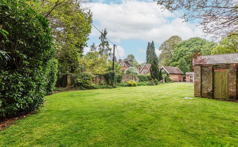 A wide striped lawn in sunshine, bounded by mature trees and hedging.