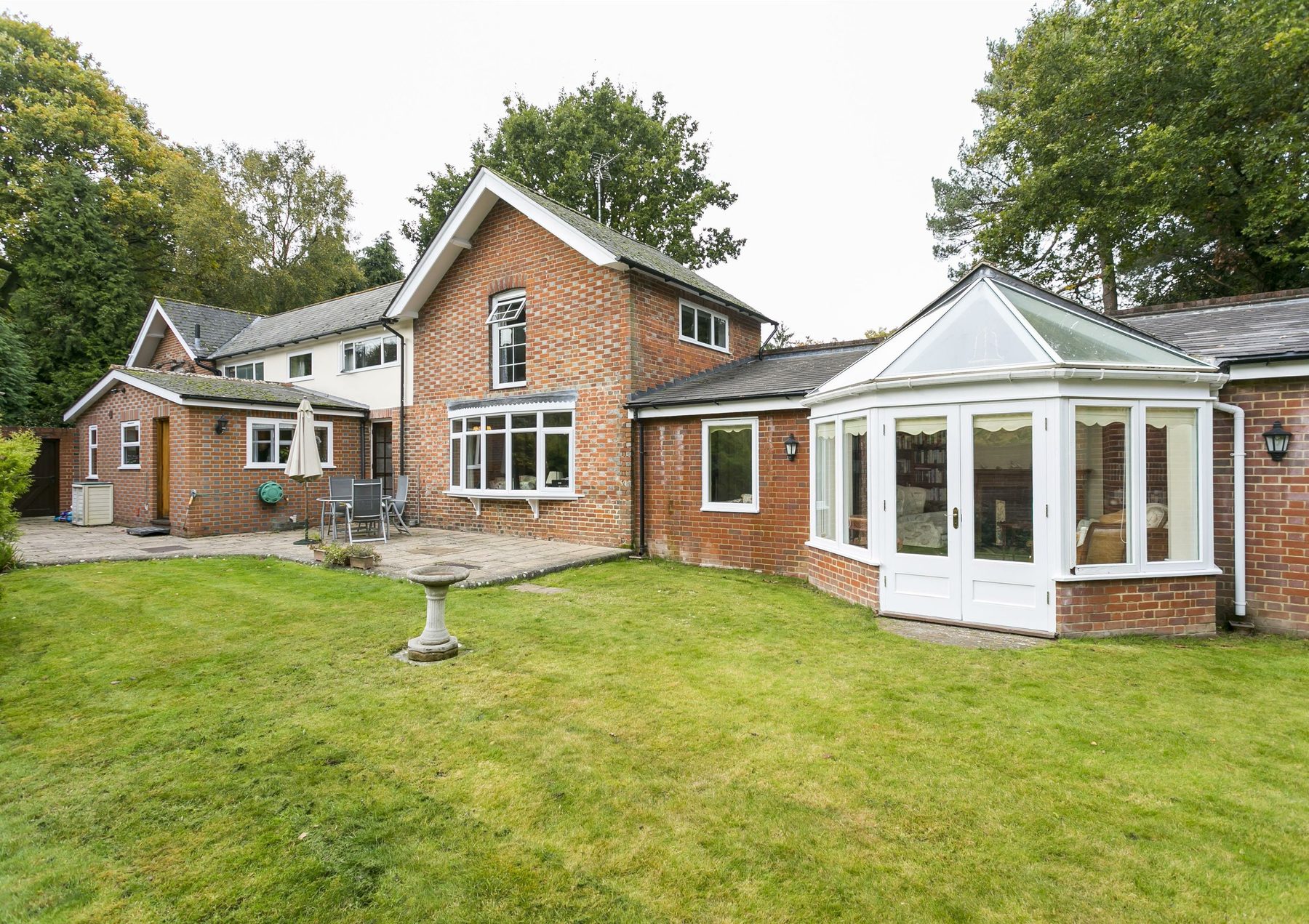The rear of Longwall House: a red-brick Victorian house with a glazed garden room, looking across a lawn to mature trees.