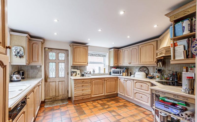 A large fitted kitchen with wooden units, tiled floor and windows on two sides.