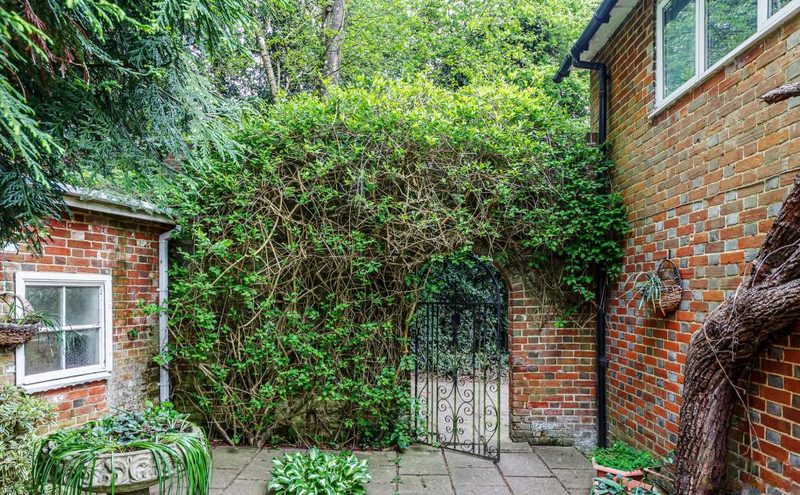 A paved courtyard enclosed by brick walls covered in climbing plants, with an iron gate.